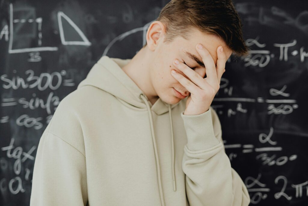 man facepalming in front of blackboard with math writing.