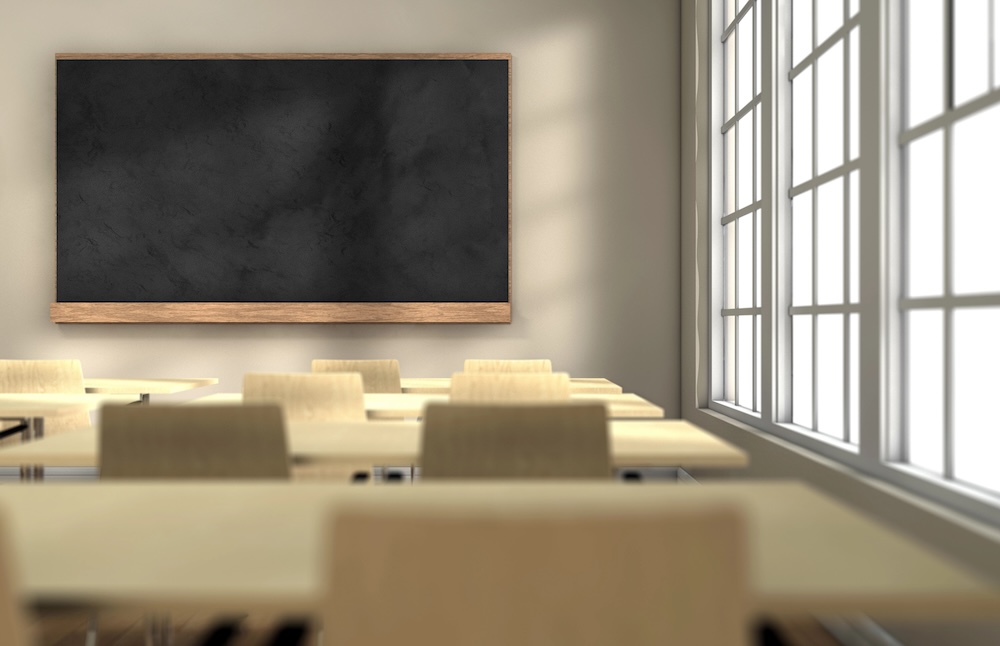 An empty classroom with a blackboard in the front, sun shining through the window.